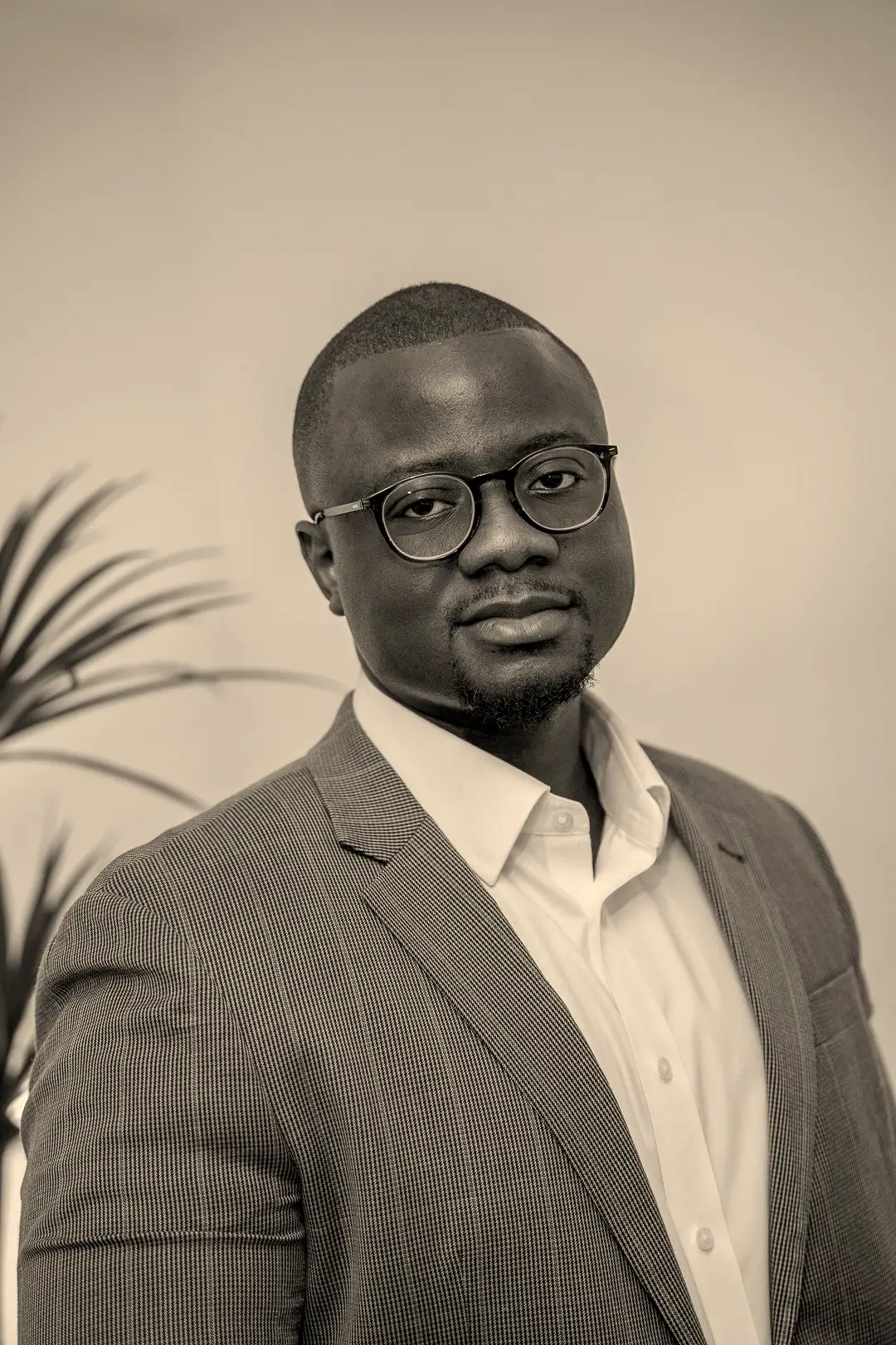 David Tandoh in a grey checked blazer and round glasses, looking straight at the camera.